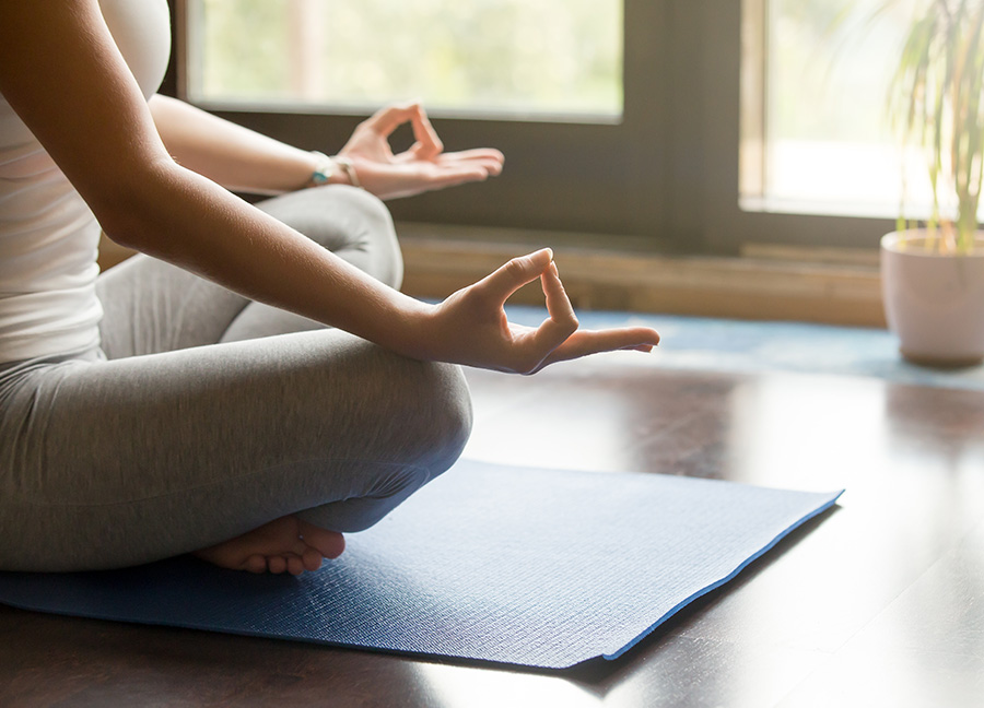 Woman in a seated yoga pose on a yoga mat in a sun-drenched room
