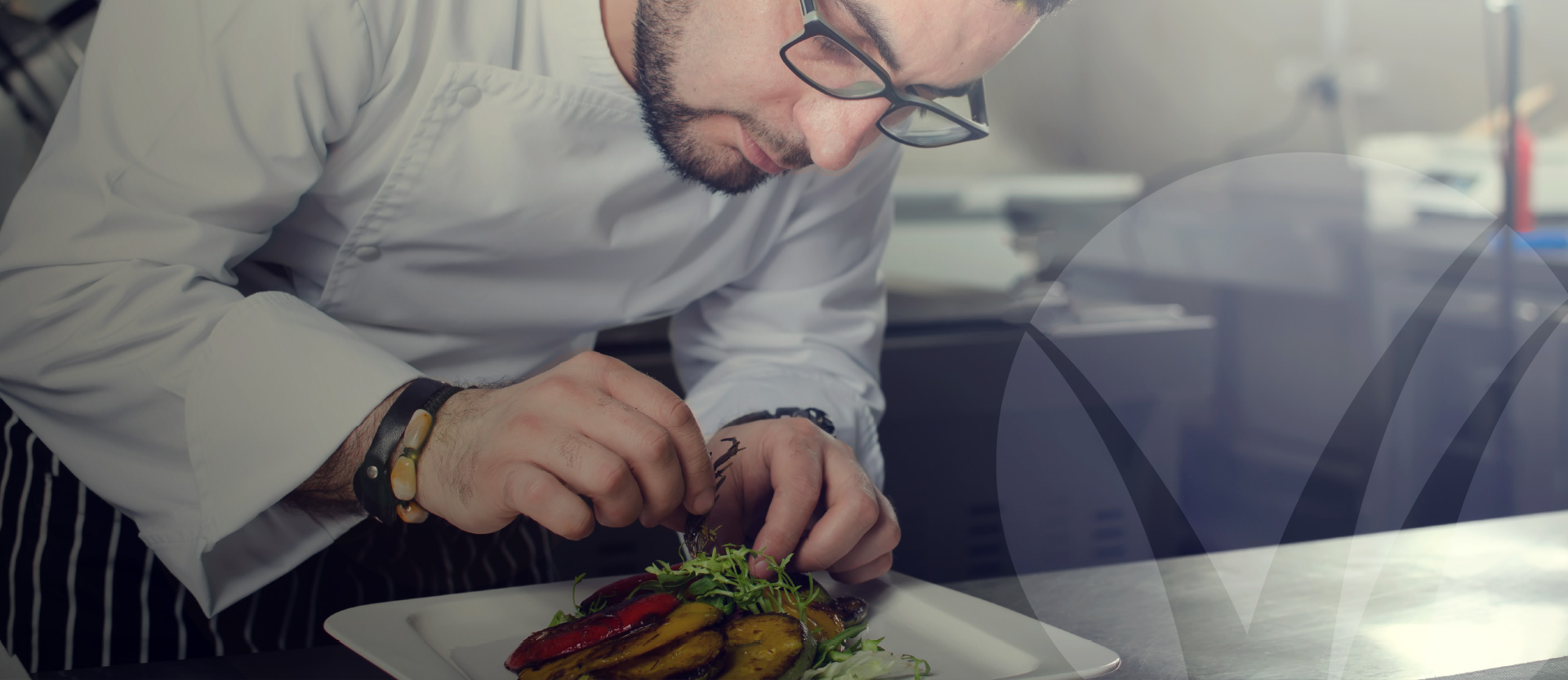 Chef wearing glasses plating a gourmet-style entree featuring fresh grilled vegetables in a professional kitchen setting. Better Homes and Gardens Real Estate