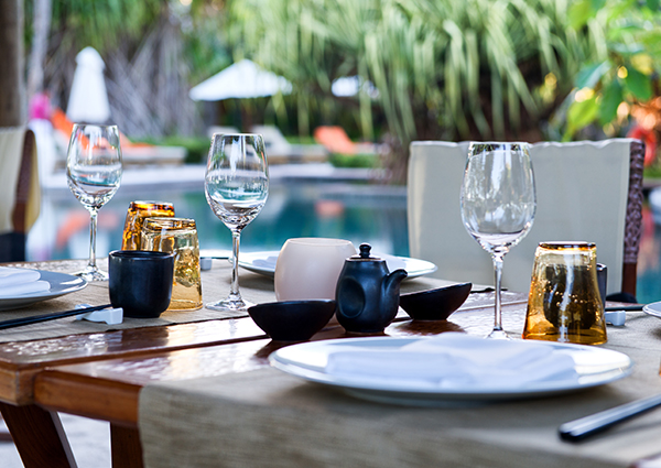 Outdoor dining table near a pool set with china and glassware