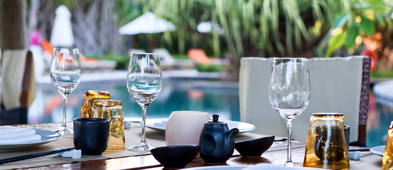 Outdoor dining table near a pool set with china and glassware
