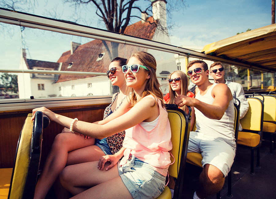 Group of young adults wearing summer outfits and sunglasses on an open-air bus taking a tour of the countryside