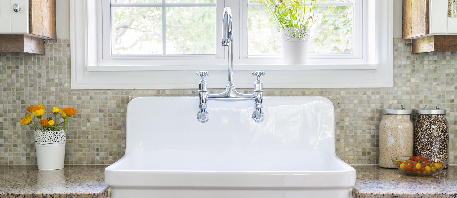 Farmhouse sink flanked by granite counter tops with a mosaic tile backsplash beneath a bright open window